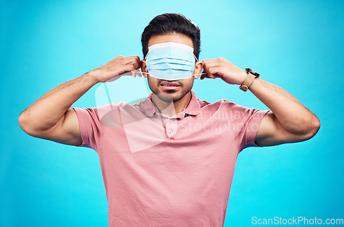 Image of Face mask, cover eyes and a man with blindfold isolated on a blue background in a studio. Struggling, virus and a person with covid wearing a tool to protect from sickness, hiding facial sight