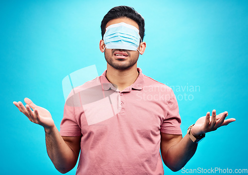 Image of Face mask, covid and man in blindfold shrugging in studio for doubt, medical misinformation or conspiracy theory. Confusion, virus or person with ppe isolated on blue background for pandemic question