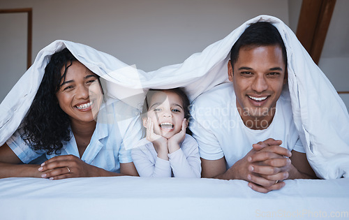 Image of Happy, love and portrait of a family on a bed in their bedroom relaxing and bonding together. Happiness, smile and girl child laying with her mother and father with a blanket in their modern home.