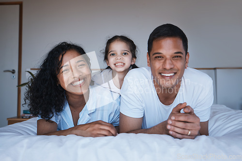 Image of Bonding, love and portrait of a family in a bedroom in their relaxing, spending quality time and bonding together. Happy, smile and girl child laying on a bed with her parents in their modern home.