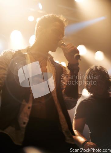 Image of Stage, light and male singer with microphone on stage or .rock and roll star at night concert. Band, music and festival for karaoke or creative performance with pop and jazz artist at indoor event