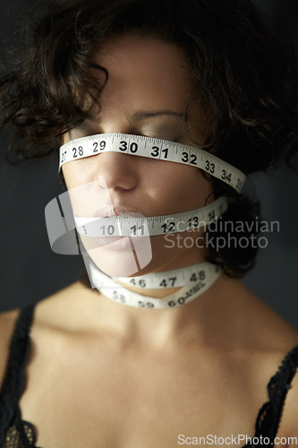 Image of Mental health. a depressed young woman with tape around face and closed eyes. Depression, a person in a black or dark background and insecure about her body with measurements covering her head.