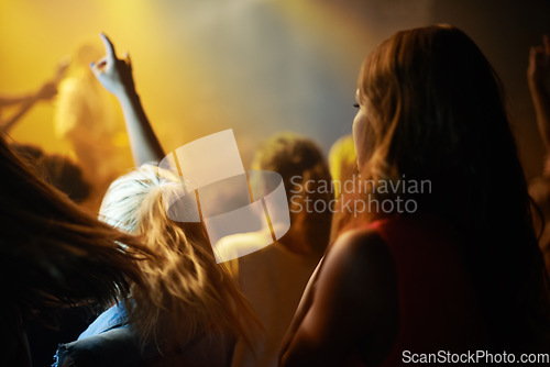 Image of Back of woman in crowd, fan at concert or music festival watching rock event on stage. Girl in audience, excited fans at live band performance in arena or stadium with lights and energy at night show