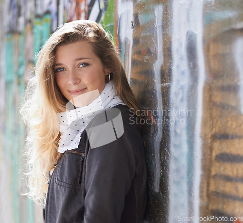 Image of Portrait, urban fashion and woman at wall with smile, graffiti and standing at outdoor street art. Happiness, youth and happy face of gen z model in city with streetwear, winter style and sunshine.