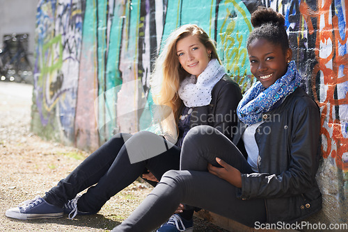Image of Stylish, women sitting outdoor at wall at campus and smiling. Young female friends, happy diverse students enjoying bonding or quality time and trendy or fashion and having fun on their day off