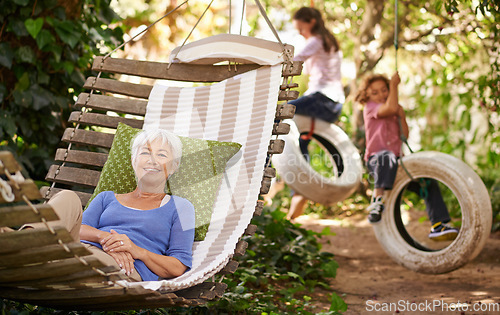 Image of Relax, happy and senior woman on a hammock while grandchildren play in the garden of the family home. Happiness, smile and portrait of elderly female person in retirement resting outdoor in backyard.