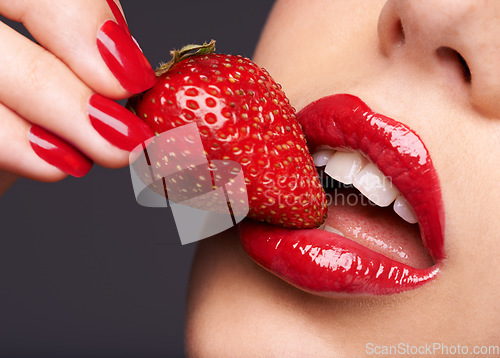 Image of Beauty, makeup and woman with a strawberry in a studio with red nails and lipstick cosmetics. Health, wellness and closeup of a female model eating fruit for nutrition isolated by a gray background.