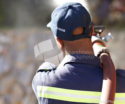 Image of Back, fireman and spray hose with water for emergency with helping, uniform and brave to stop inferno. Firefighter, fire and fearless on mission for rescue, health and safety service at job outdoor