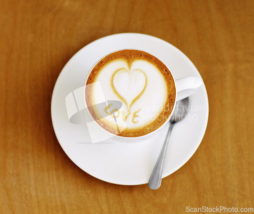 Image of Coffee cup, cappuccino and heart in foam on a table with no people in a restaurant and diner. Cafe drink, love writing and foamy beverage art with milk in a cafe with a closeup of mug and spoon