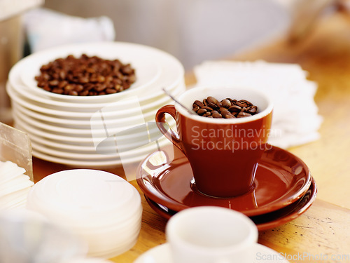 Image of Cup, roasted coffee beans and cafe industry or shop with quality product for marketing or catering. Texture, abstract or background with brown grain as drink, espresso or caffeine ingredient on table