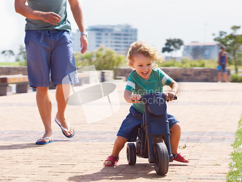 Image of Happy, toy and motorbike with child and father playing in park for bonding, laugh and fun. Smile, happiness and energy with man and young boy riding on scooter for playful, youth and summer