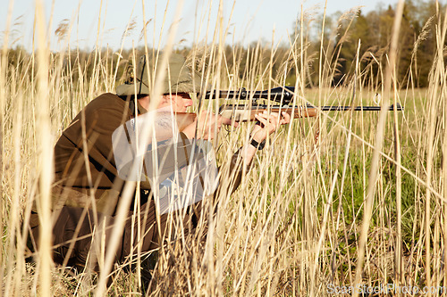 Image of Nature, hunter and man with a rifle while in camouflage shooting in outdoor field. Grass, wildlife and male sniper hunting animals with shotgun weapon hiding in plants to shoot target in countryside.