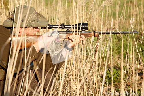 Image of Nature, wildlife and male hunter with a shotgun while in camouflage shooting in outdoor field. Grass, safari and man hunting animals with rifle weapon hiding in plants to shoot target in countryside.