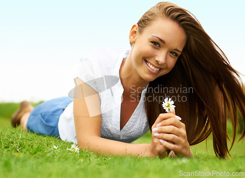 Image of Portrait, smile and woman with daisy on grass, lying down on field and enjoying spring on vacation outdoor. Happy, flower plant and beauty of female person relaxing, smiling and having fun in nature.