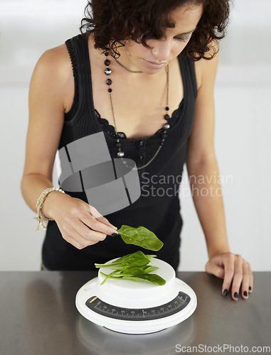 Image of Woman, scale and spinach in kitchen for food, diet or eating disorder with leaves for meal plan. Girl, mental health and vegetable leaf to lose weight with anorexia, bulimia or starving in house