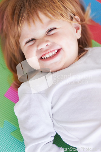 Image of Young girl, laughing and happiness portrait of a baby on a home playpen ground with a smile. Ginger infant, kid laugh and happy in a house with joy, youth and positivity from childhood looking up