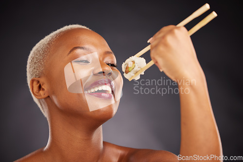 Image of Face, eating and woman with sushi and chopsticks in studio for healthy food or beauty. Black female model with makeup on a dark background for wellness glow, fish diet or seafood with nutrition