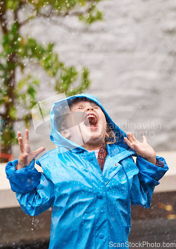 Image of Wet weather, raincoat and a girl playing in the rain outdoor alone, having fun during the cold season. Kids, winter or freedom with an adorable little female child standing arms outstretched outside