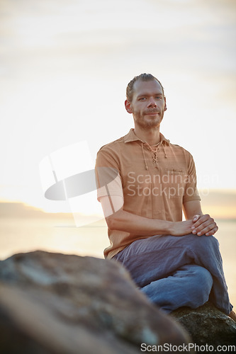 Image of As tranquil and peaceful as nature. Shot of a peaceful man sitting on a rock at the beach.