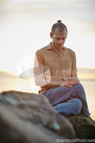 Image of Calm and collected just as nature intended. Shot of a peaceful man sitting on a rock during his yoga routine at the beach.