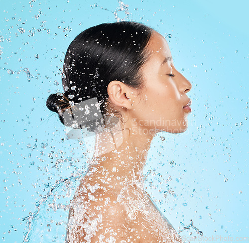 Image of Beauty, water and face profile of woman on blue background for wellness, healthy skin and cleaning. Bathroom, shower and female person with splash for facial grooming, washing and skincare in studio