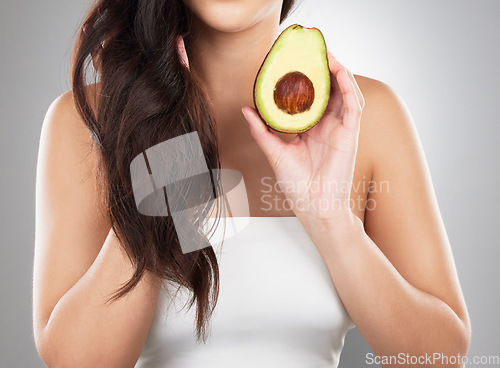 Image of Hair care, wellness and woman with an avocado in a studio for a natural, organic or health mask. Self care, beauty and closeup of a female model with a fruit for a hair treatment by a gray background