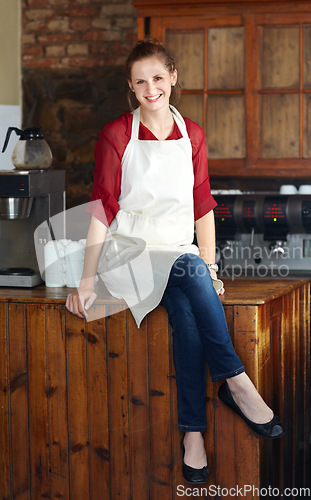 Image of Woman in portrait, barista at coffee shop and sit on countertop, happy employee in hospitality industry. Female professional in cafe, small business owner and entrepreneur smile with positive mindset