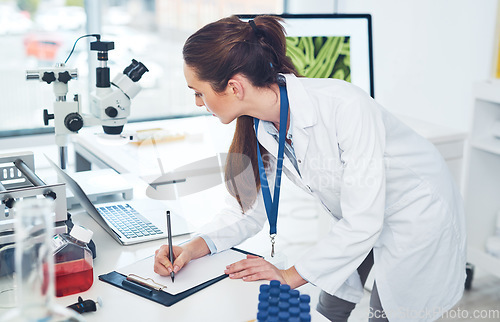 Image of I have to right down everything I see. Cropped shot of a focused young female scientist making notes in a book while doing tests inside of a laboratory during the day.