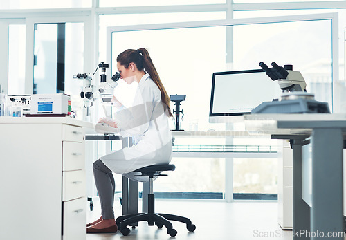 Image of Paying close attention to detail. Cropped shot of a focused young female scientist looking through a microscope while doing tests inside of a laboratory.