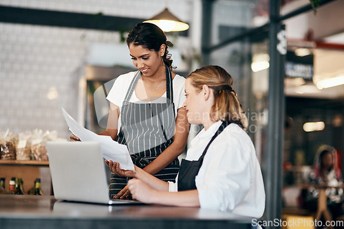 Image of A connected team keeps the numbers up. Shot of two women using a laptop together while working in a cafe.