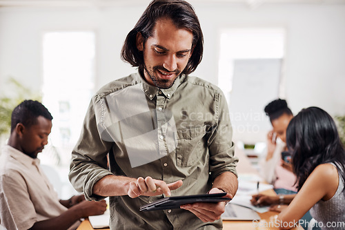 Image of Surfing the web for some inspiration. Shot of a young businessman using a digital tablet in an office with his colleagues in the background.