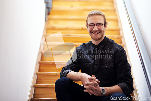 Image of I am happy with my career choice. Cropped portrait of a handsome young businessman sitting alone on the wooden staircase in his office.