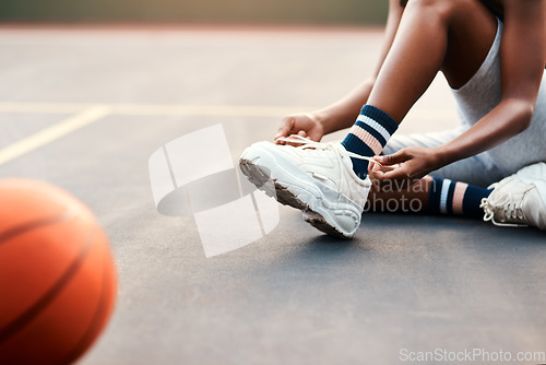 Image of I dont want to trip of the court. Cropped shot of an unrecognizable sportswoman sitting on the court and tying her shoelaces before playing a game of basketball.