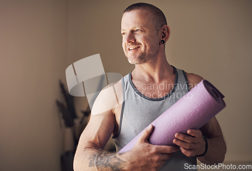 Image of Yoga helps me slow down and appreciate life. Cropped shot of a handsome young man standing alone and holding his yoga mat before an indoor yoga session.