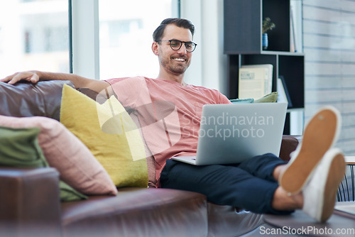 Image of High website traffic makes a happy entrepreneur. Shot of a young man using a laptop while relaxing on a sofa.