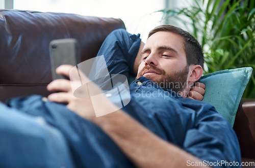 Image of Recharge and bounce back better than ever. Shot of a young man using a smartphone while relaxing on a sofa.