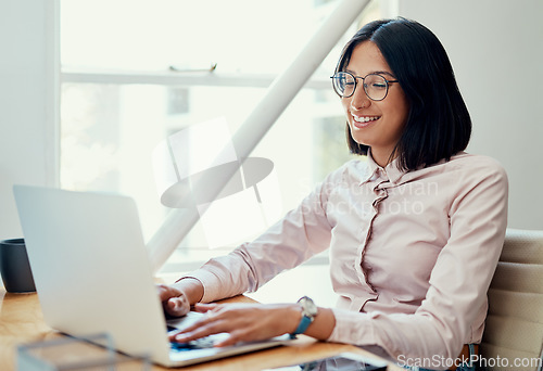 Image of Working through my day with a smile. Cropped shot of an attractive young businesswoman sitting alone and using her laptop in the office.