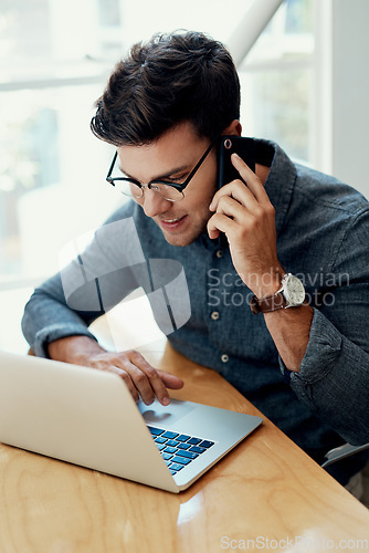 Image of Let me check that for you. Cropped shot of a handsome young businessman sitting and using his cellphone while working on his laptop in the office.