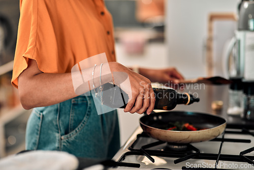 Image of Hands, cooking and olive oil with a woman in the kitchen of her home for food or meal preparation. Stove, pan and container with a female chef in her house to cook for health, diet or nutrition