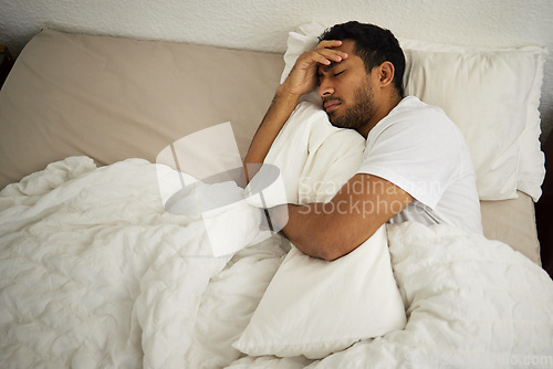 Image of Sleeping problem, headache and man in bed with pillow at home with insomnia and fatigue. Morning, male person and house feeling frustrated and sad from pain and sleep issue with blanket in bedroom