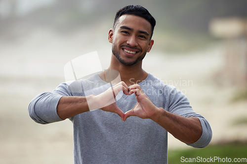 Image of Portrait of happy man, heart and hand outdoor for care, kindness and emoji for charity, mental health and joy. Young guy, self love and finger shape of hands for thank you, trust and hope with smile