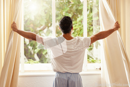 Image of Back view, man and open curtain at window to good morning, sunrise and sunshine to relax in room at home. Guy, wake up and opening bedroom drapes in apartment for sunlight, fresh air or start new day