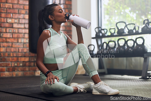 Image of Woman, tired and drinking water on floor at gym in workout, training or exercise for fitness, health or wellness. Young indian girl, bottle and hydration for body development, commitment or hard work