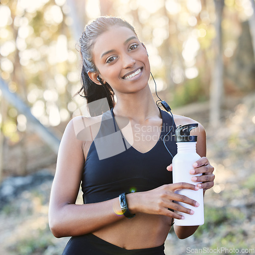 Image of Fitness, portrait and woman with a bottle in the woods after running for race or marathon training. Sports, earphones and female athlete listening to music for cardio workout with water for hydration