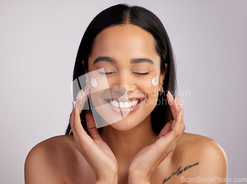 Image of Happy woman, face and smile with cream for skincare, beauty or cosmetics against a grey studio background. Female person or model smiling for lotion, creme or cosmetic moisturizer or facial treatment