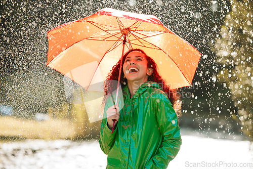 Image of Funny, nature or happy woman with an umbrella in rain for insurance or covering in city outdoors. Smile, happiness or wet girl laughing with tools for winter cover, protection and walking in a park