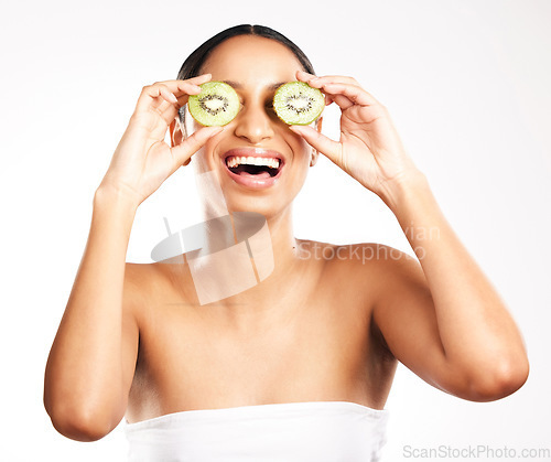 Image of Happy woman, face and kiwi for vitamin C, skincare or diet against a white studio background. Female person or model with smile and natural fruit for healthy nutrition, collagen or facial treatment