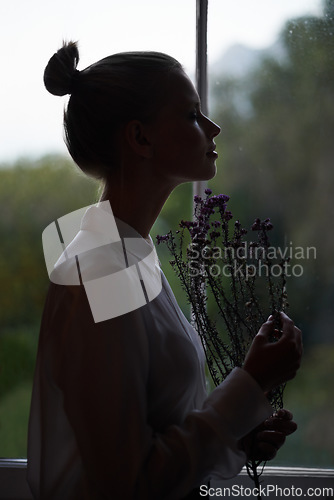 Image of Dawn beauty. A silhouette of a beautiful young woman holding some flowers and enjoying their scent.