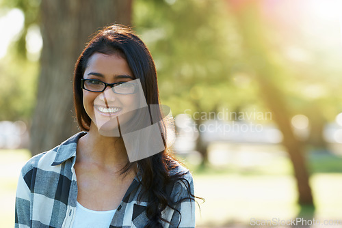 Image of Relaxed beauty. A beautiful young woman wearing glasses standing in a park.