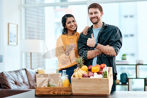 Image of Good health is the way to go. Shot of a happy young couple showing thumbs up after unpacking their healthy groceries at home.